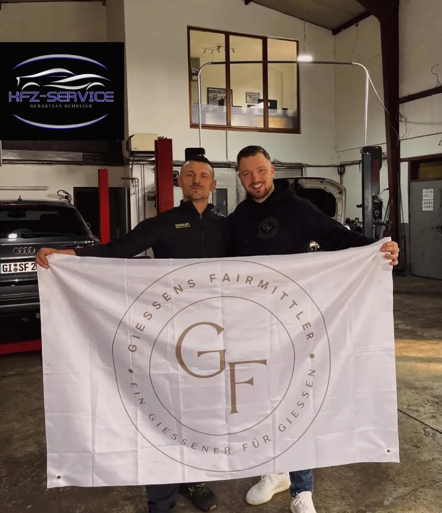 Sebastian Schreier und Leon Konrad halten in der Werkstatt die Flagge von Gießens Fairmittler